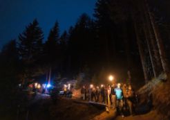 Eine Gruppe von Leuten wandert im Dunkeln mit Fackeln den Berg hinab.
