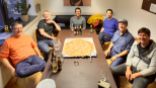 Sechs Drupal-Entwickler der User Group Bodensee sitzen um einen Tisch, in der Mitte liegt eine große Pizza